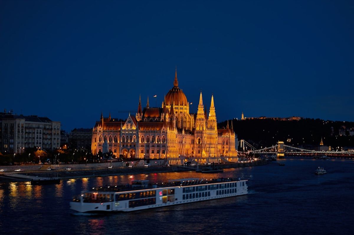 A river cruise ship passing the Budapest Parliament at night
